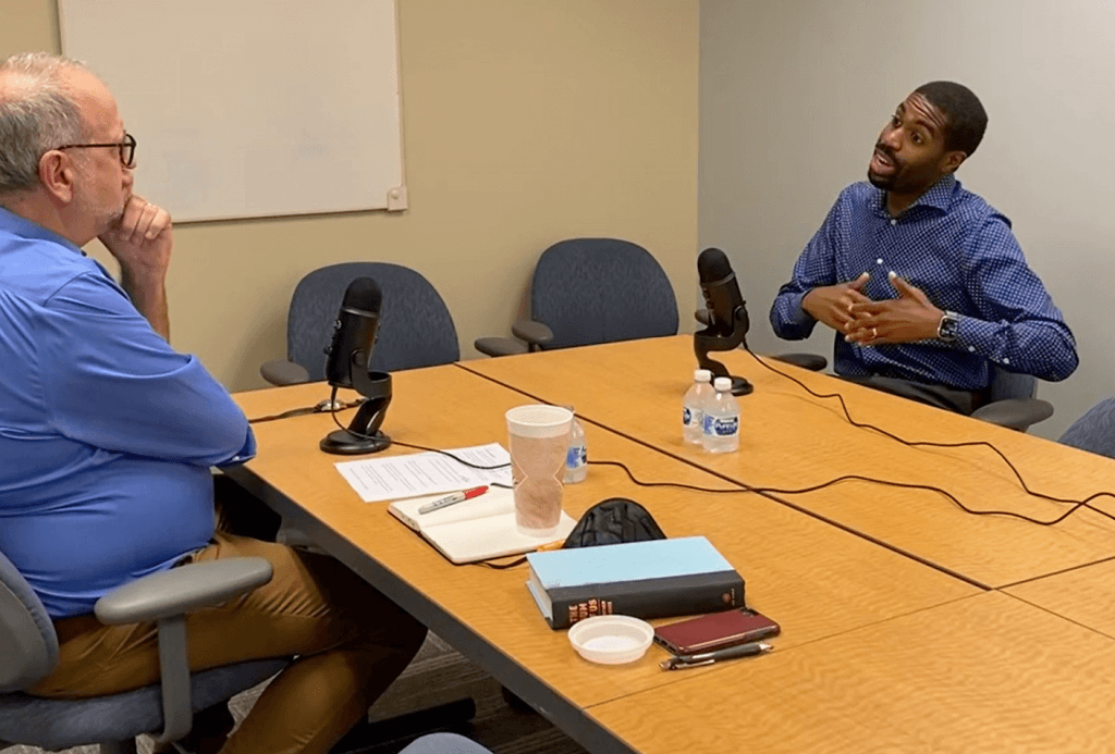 Stuart Comstock-Gay and Arreon Harley-Emerson seated at a conference room table with microphones. Arreon is speaking.